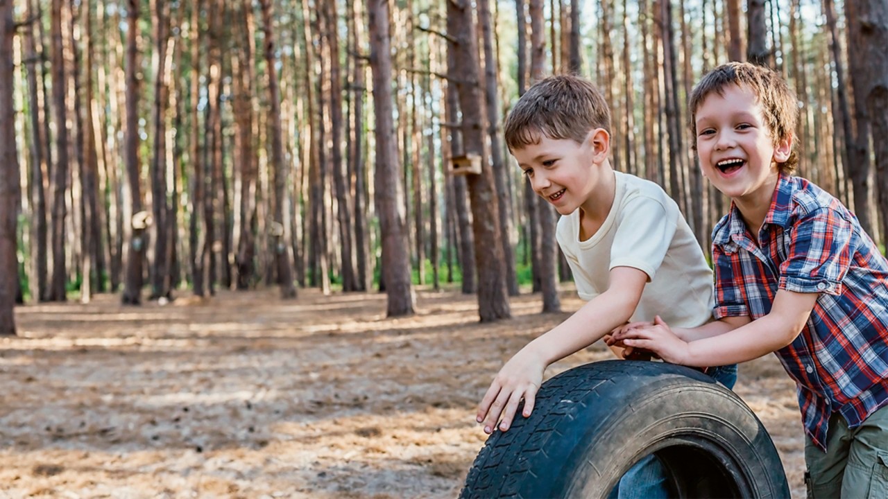Happy children playing with a tire in the woods
