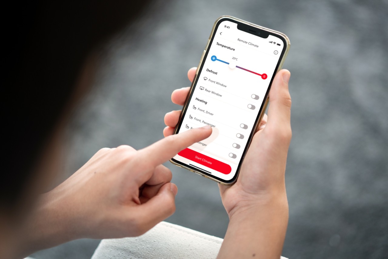 Oseba drži pametni telefon, na katerem je prikazana aplikacija MyToyota. Njena leva roka tapka po zaslonu, da na daljavo nastavi klimatsko napravo v avtomobilu.